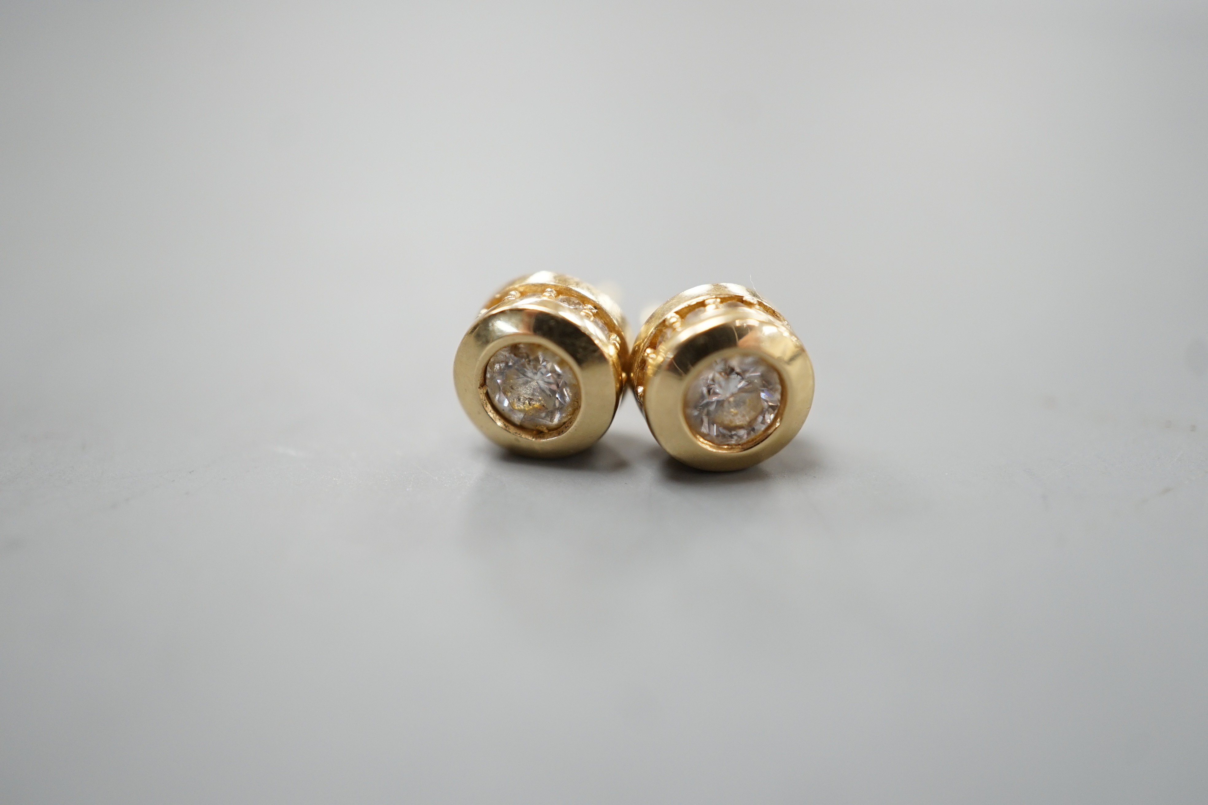 A modern pair of 14k yellow metal and single stone diamond set ear studs, with diamond chip setting, diameter 6mm, gross weight 2.8 grams.